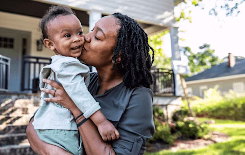 A woman kisses her child in front of their house
