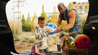 A boy and his father getting a ball out from the trunk of their car
