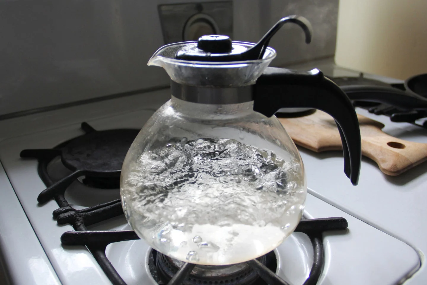 Hervidor de vidrio hirviendo agua en una estufa de gas con burbujas y vapor visibles.