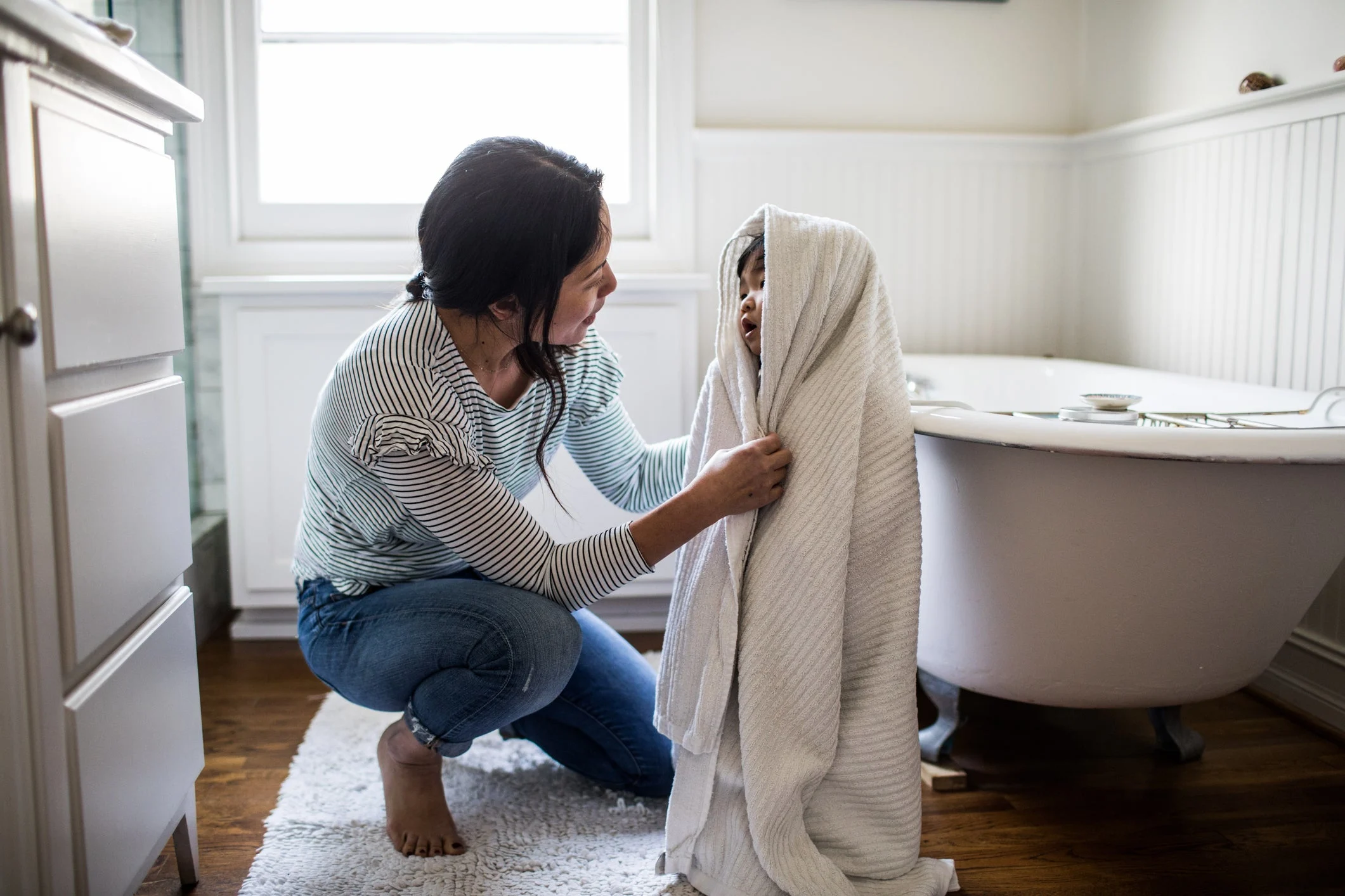 Mamá secando a un niño pequeño en el baño con una toalla blanca grande.
