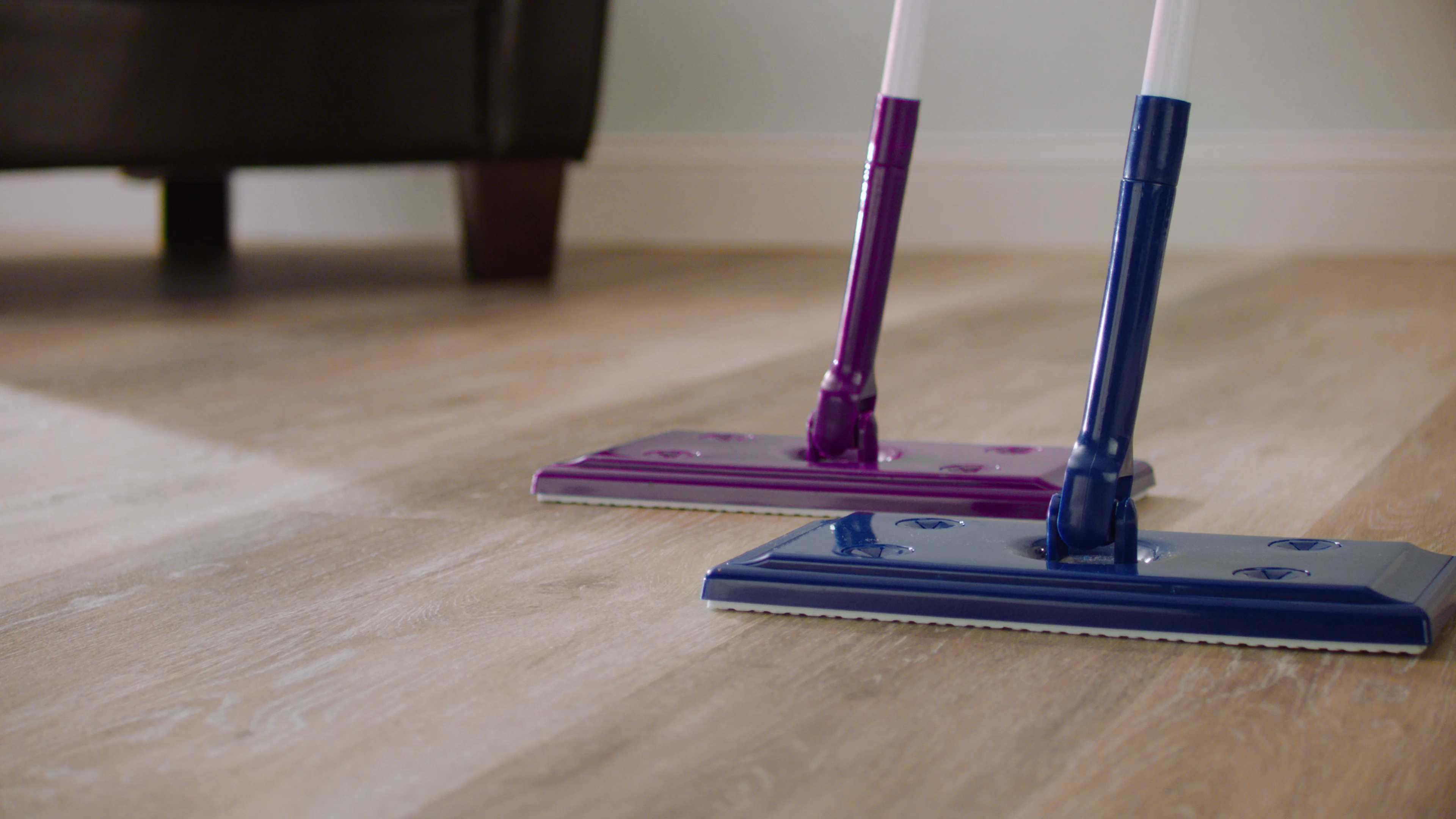 Purple and blue mop tools on wood floor, chair in background.