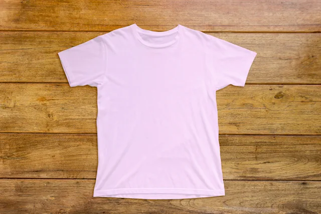 A clean, light pink short-sleeved T-shirt lies flat on a hardwood floor.