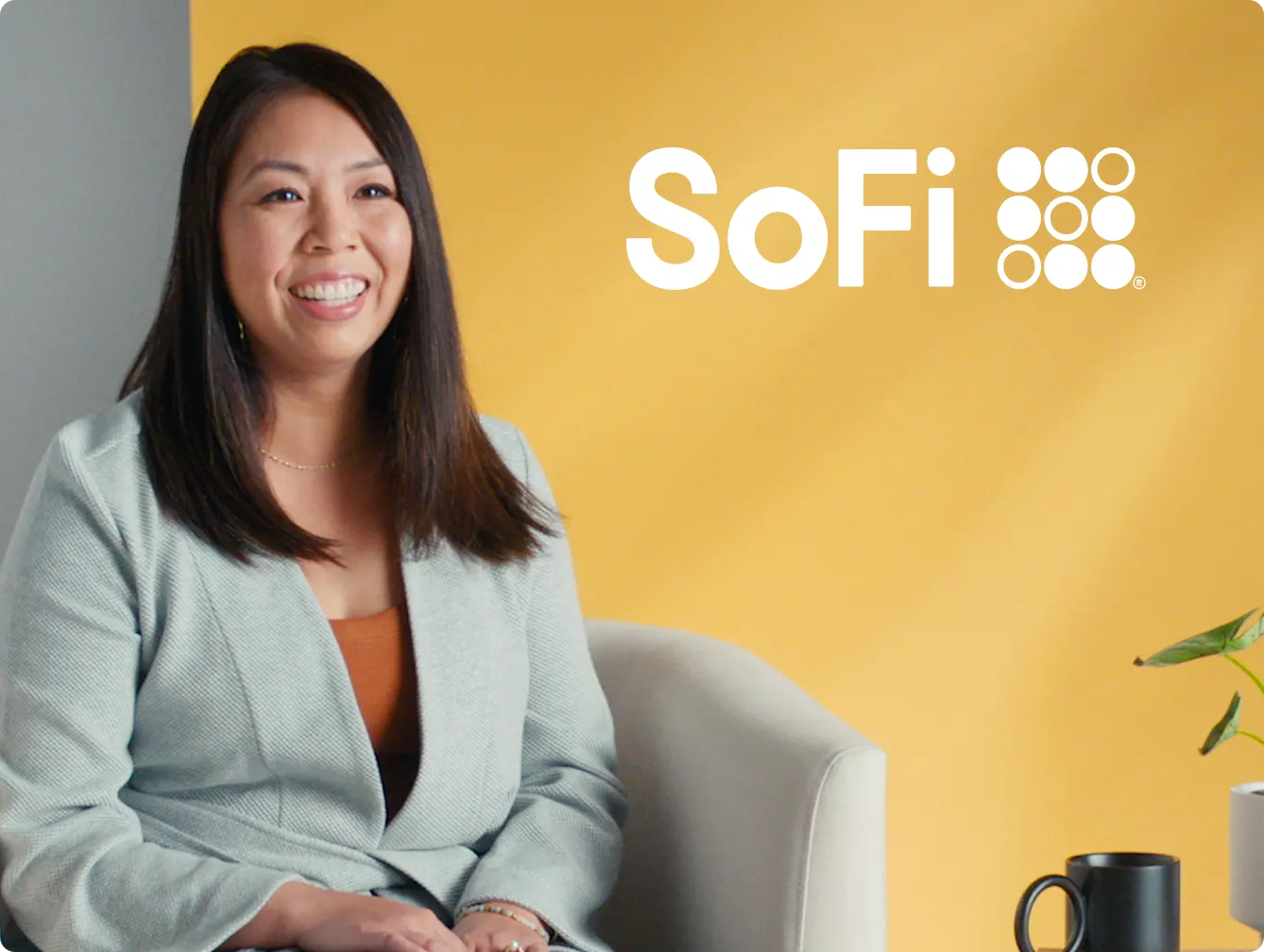 SoFi advertisement featuring a smiling woman with long dark hair, wearing a light gray blazer and an orange top, sitting on a chair. Next to her is a small table with a plant and a black mug. The SoFi logo is prominently displayed at the top right of the image on a yellow background.