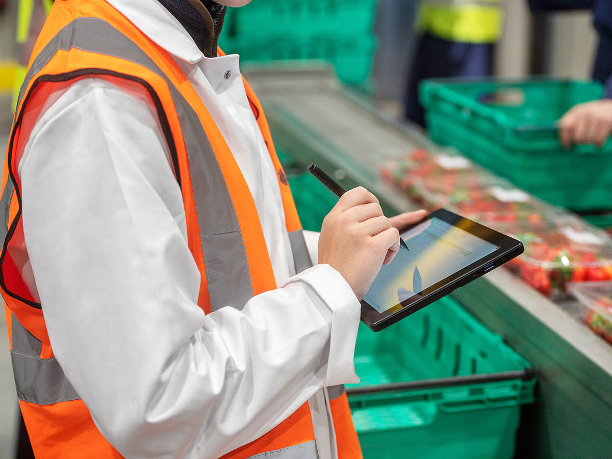 A man in an orange vest is using a tablet to access food safety software.